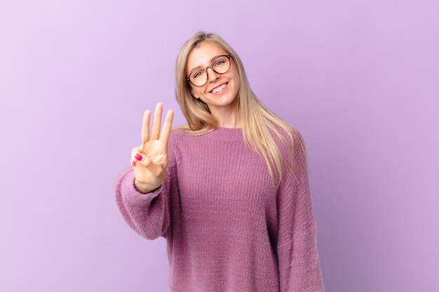 Jovem loira sorrindo e parecendo amigável, mostrando o número três