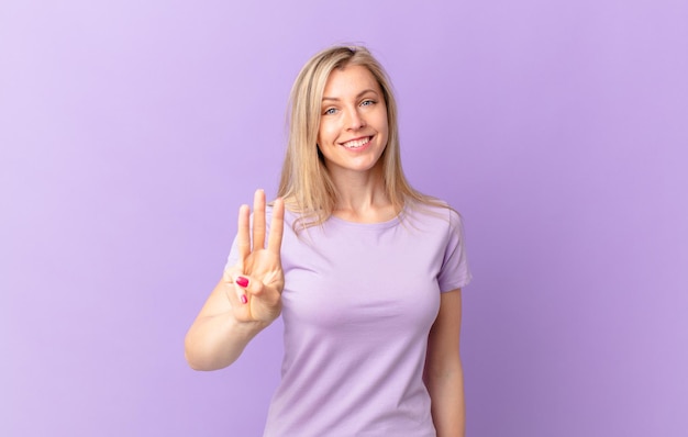 Jovem loira sorrindo e parecendo amigável, mostrando o número três