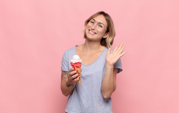 Jovem loira sorrindo feliz e animada, acenando com a mão, dando as boas-vindas e cumprimentando você ou dizendo adeus