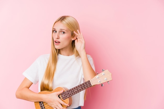 Jovem loira tocando cavaquinho tentando ouvir uma fofoca.