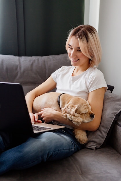 Jovem loira trabalhando online em um laptop com um spaniel sentado em seu colo