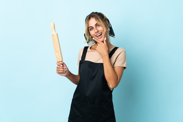 Jovem loira uruguaia cozinhando isolada em uma parede azul feliz e sorridente
