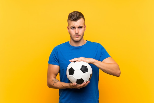 Jovem loiro bonito segurando uma bola de futebol