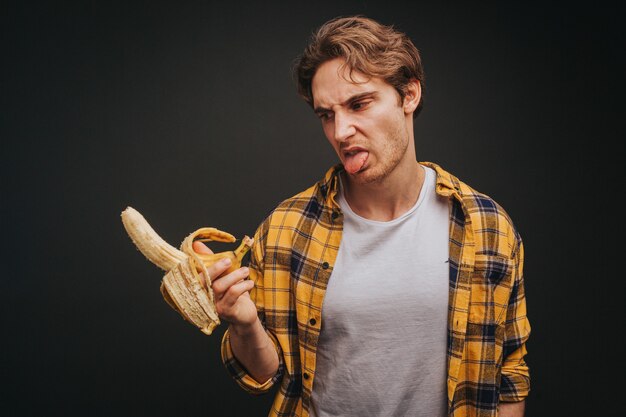 Jovem loiro de camisa amarela comendo banana com relutância