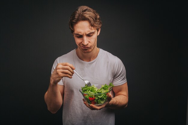 Foto jovem loiro de camiseta branca segurando o prato de salada com a decepção