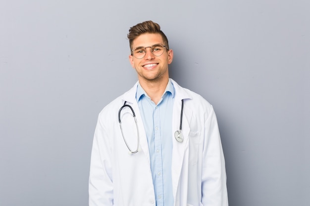 Jovem loiro médico homem feliz, sorridente e alegre.