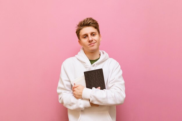 Jovem loiro segurando o livro na mão isolado no fundo rosa