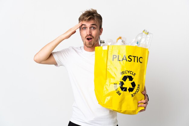 Jovem loiro segurando um saco de reciclagem cheio de papel para reciclar isolado no fundo branco percebeu algo e tenciona encontrar a solução