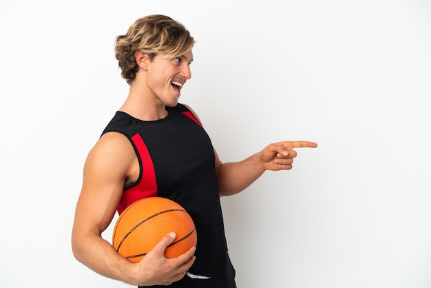 Jovem loiro segurando uma bola de basquete isolada no branco apontando o dedo para o lado e apresentando um produto