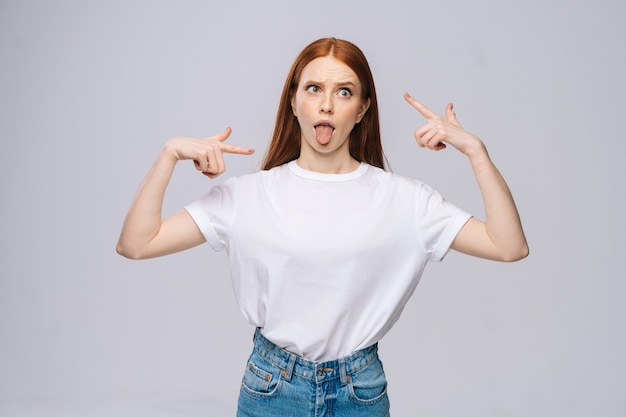 Jovem louca e feliz vestindo camiseta e calça jeans mostrando a língua em fundo branco isolado