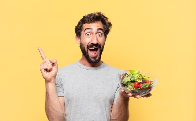 Jovem louco barbudo fazendo dieta comemorando uma vitória bem-sucedida e segurando uma salada