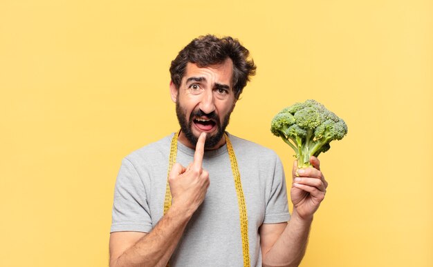 Jovem louco barbudo fazendo dieta e expressão triste e segurando um repolho