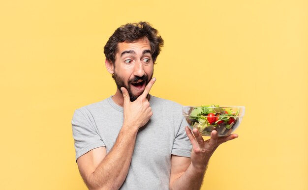 Jovem louco barbudo fazendo dieta, expressão de pensamento e segurando uma salada