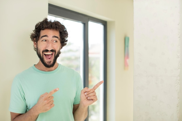 jovem louco barbudo sorrindo alegremente e apontando para copiar o espaço na palma da mão ao lado, mostrando ou anunciando um objeto