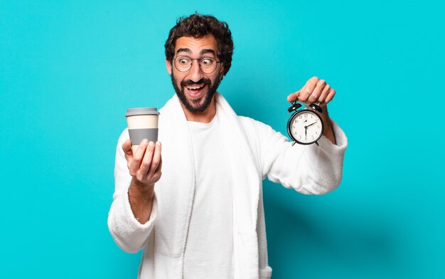 Jovem louco de barba usando roupão de banho e despertador