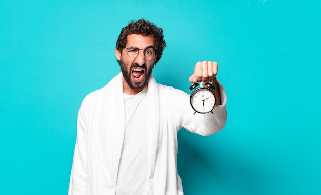 Jovem louco de barba usando roupão de banho e despertador