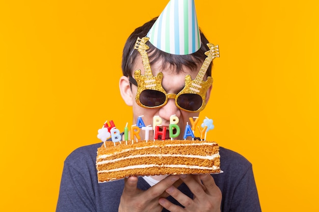 Jovem louco e alegre de óculos e chapéus de felicitações de papel segurando um bolo