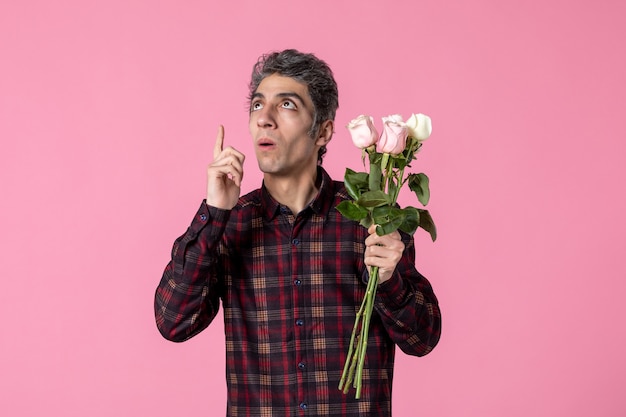 Jovem macho com lindas rosas cor de rosa na parede rosa