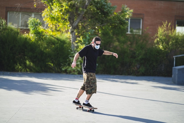 Jovem macho fazendo truques diferentes com um skate no parque usando uma máscara facial de médico