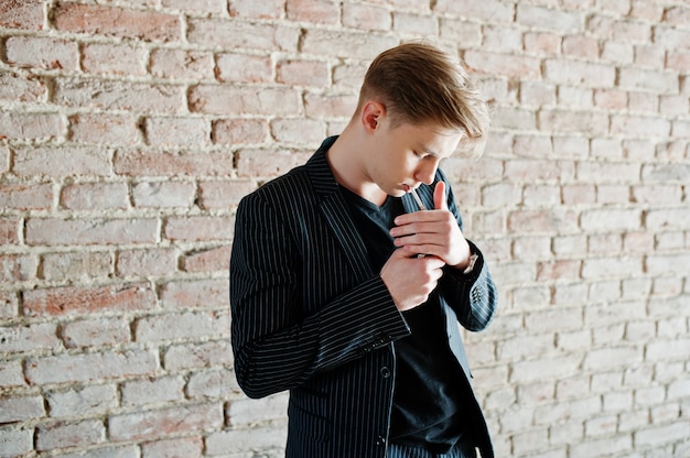 Jovem macho macho usar blac elegante casaco fumar cigarro nas ruas.