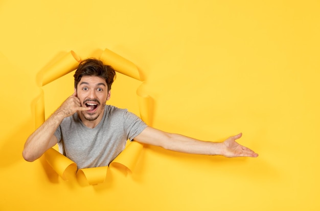 Jovem macho olhando de fundo de papel amarelo rasgado dentro de casa venda facial