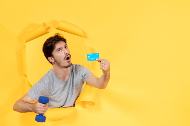 jovem macho segurando cartão de crédito e halteres no fundo amarelo dinheiro de treino apto para atleta