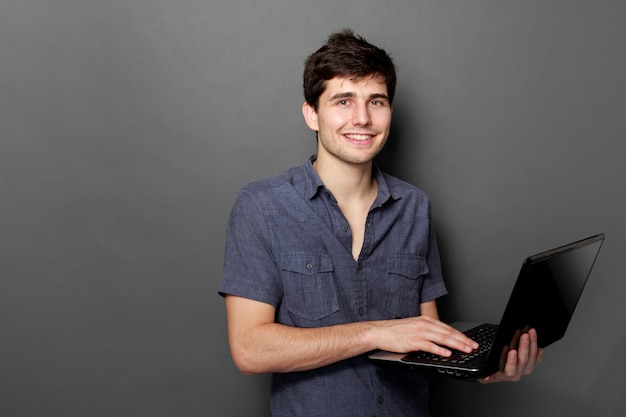 Jovem macho sorrindo usando computador portátil
