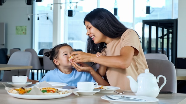 Jovem mãe a segurar uma fatia de pizza e a menina a comer a brincar