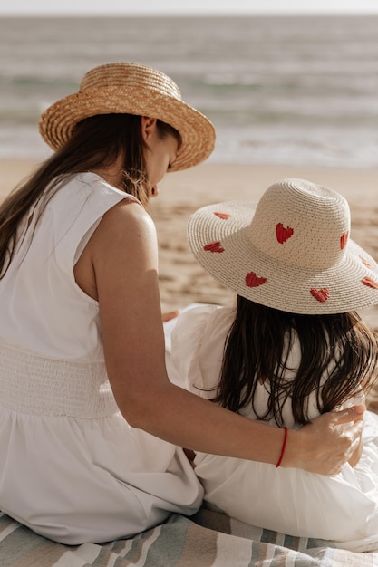 Jovem mãe abraçando a filha na praia arenosa ao pôr do sol