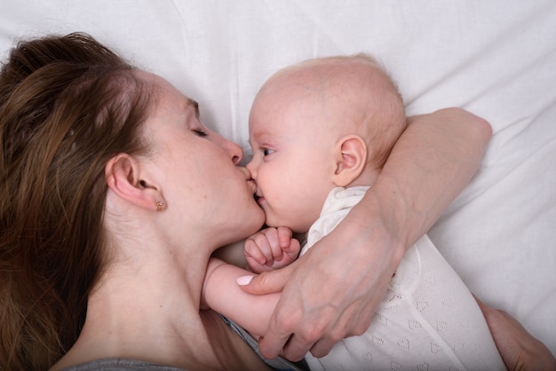 Jovem mãe abraçando e beijando bebê. Amor de mãe, maternidade, paternidade