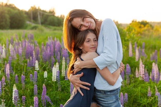 Jovem mãe abraçando seu filho ao ar livre Mulher e adolescente no campo de verão com flores silvestres desabrochando fundo verde Família feliz mãe e filha brincando no prado