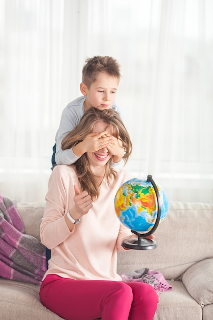 Jovem mãe ajudando seu filho a fazer a lição de casa. Família, escolhendo para onde viajar de férias. Mãe e filha segurando um globo