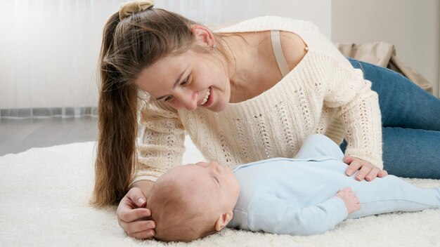 Foto jovem mãe amorosa acariciando e conversando com seu filho deitado no tapete na sala de estar