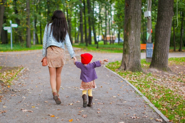 Jovem mãe andando com sua filha no parque outono