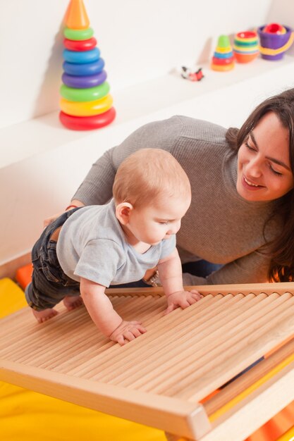 Jovem mãe apóia o bebê, ajudando-o a subir a escada no jardim de infância