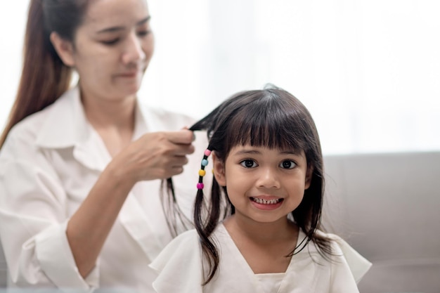 Jovem mãe asiática amarrando o cabelo da filha