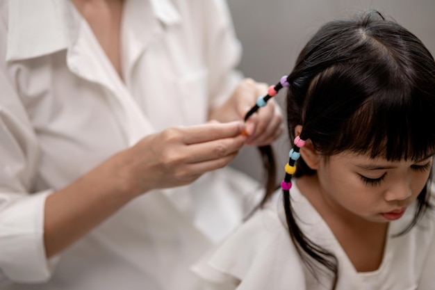 Jovem mãe asiática amarrando o cabelo da filha