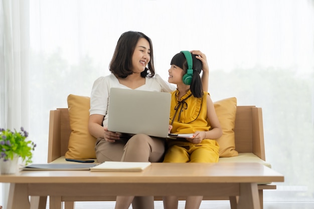 Jovem mãe asiática com laptop ensinando criança a aprender ou estudar online em casa