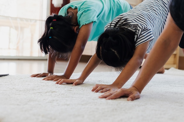 Jovem mãe asiática e suas filhas fazendo alongamento e ioga exercícios de fitness juntos em casa. Pais e filhos exercem-se para serem fortes e manter a saúde física e o bem-estar na rotina diária.