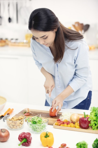 Jovem mãe asiática fazendo comida na cozinha com uma cara de sorriso.