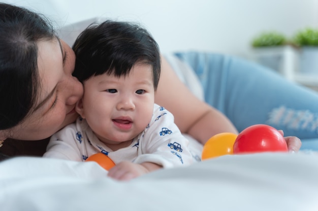 Jovem mãe asiática linda com bebê asiático na cama