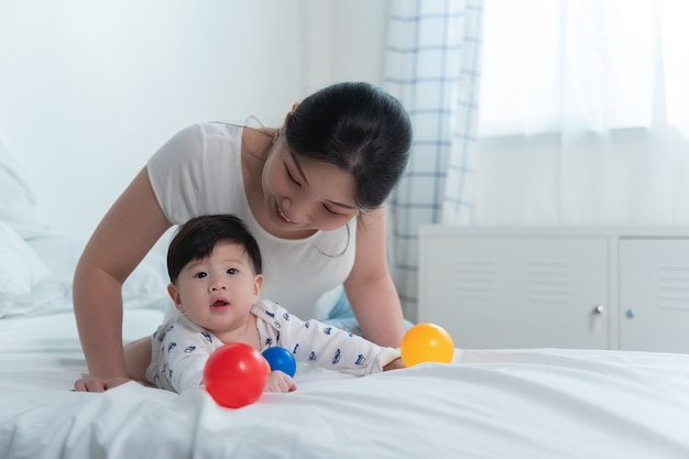 Jovem mãe asiática linda com bebê asiático na cama