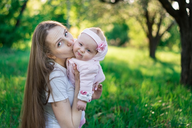 Jovem mãe beijando bebê no parque natural. Passeio no parque com o bebê.