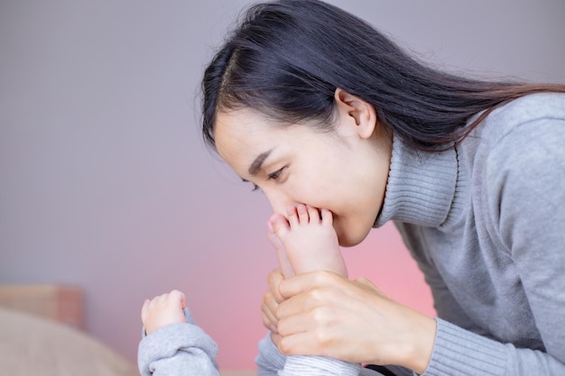 jovem mãe beijando pezinhos de bebê na cama