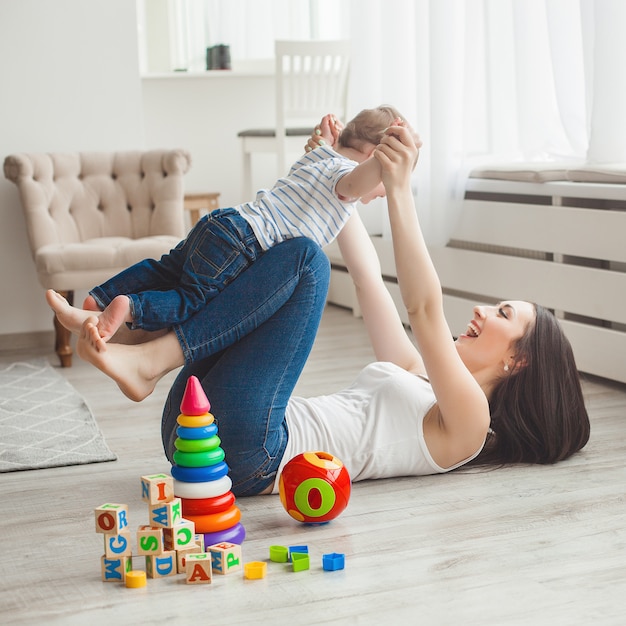 Foto jovem mãe bonita brincando com seu filho pequeno. família alegre se divertindo dentro de casa com o filho bebê