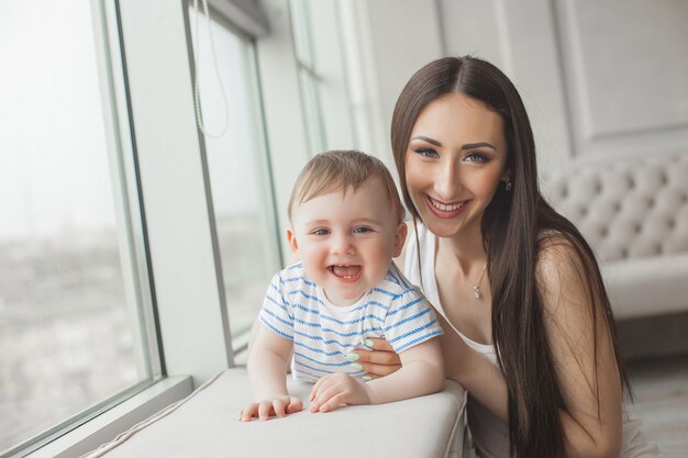 Jovem mãe bonita brincando com seu filho pequeno. Família alegre, sorrindo para a câmera