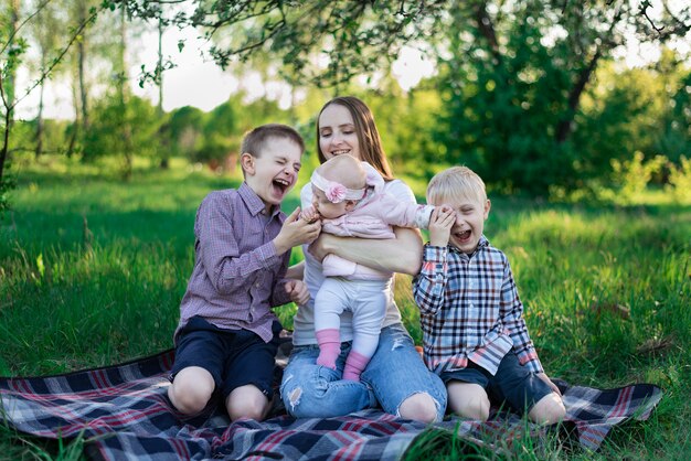 Jovem mãe bonita com filha e dois filhos na manta no parque. Riso das crianças, infância feliz