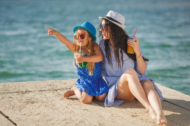 Jovem mãe bonita e sua filha na praia se divertindo. meninas bebendo limonada.