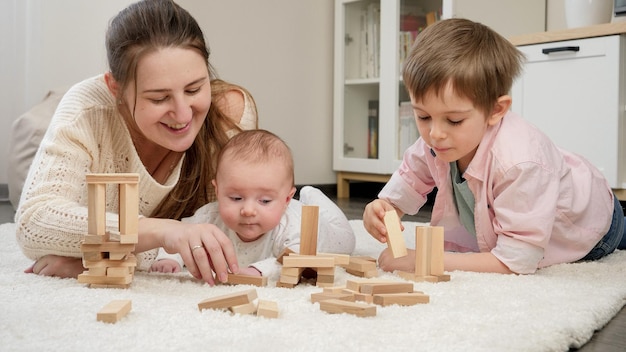 Jovem mãe brincando com seus filhos pequenos no tapete da sala de estar criando felicidade para os filhos