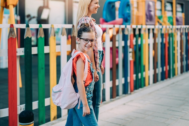 Jovem mãe caminhando com sua filha para a escola primária. De volta ao conceito de escola.